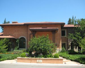 Residential stucco roof tan house with bush in front of the entryway